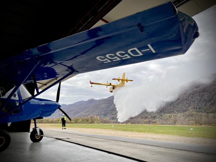 Ala del Savannah I-D555 in hangar mentre un Canadair sgancia acqua durante un'esercitazione antincendio DOS