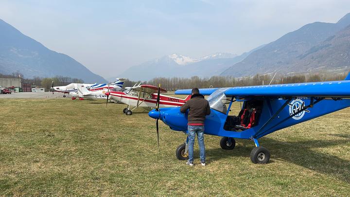 Pilota accanto al Savannah con altri ultraleggeri allineati all'aviosuperficie di Caiolo, con le montagne innevate sullo sfondo