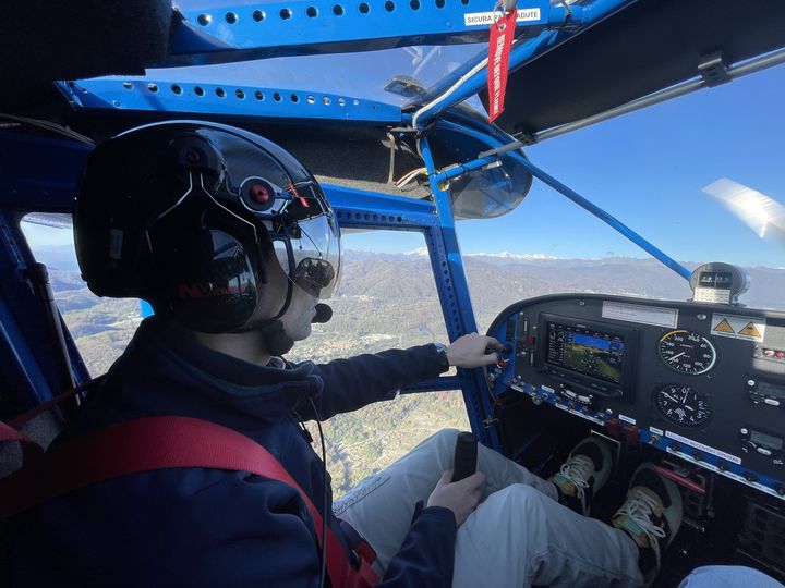 Pilota con casco ai comandi del Savannah sopra le colline, con le Alpi innevate davanti al parabrezza