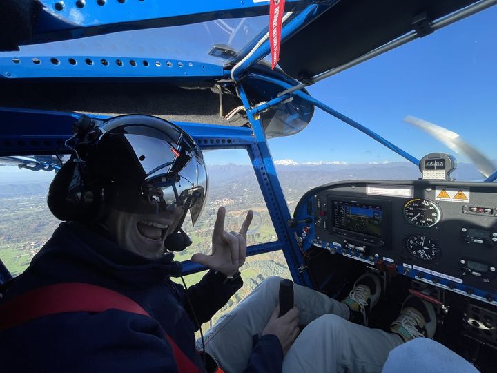 Pilota sorridente con casco in cabina del Savannah, con le Alpi innevate all'orizzonte